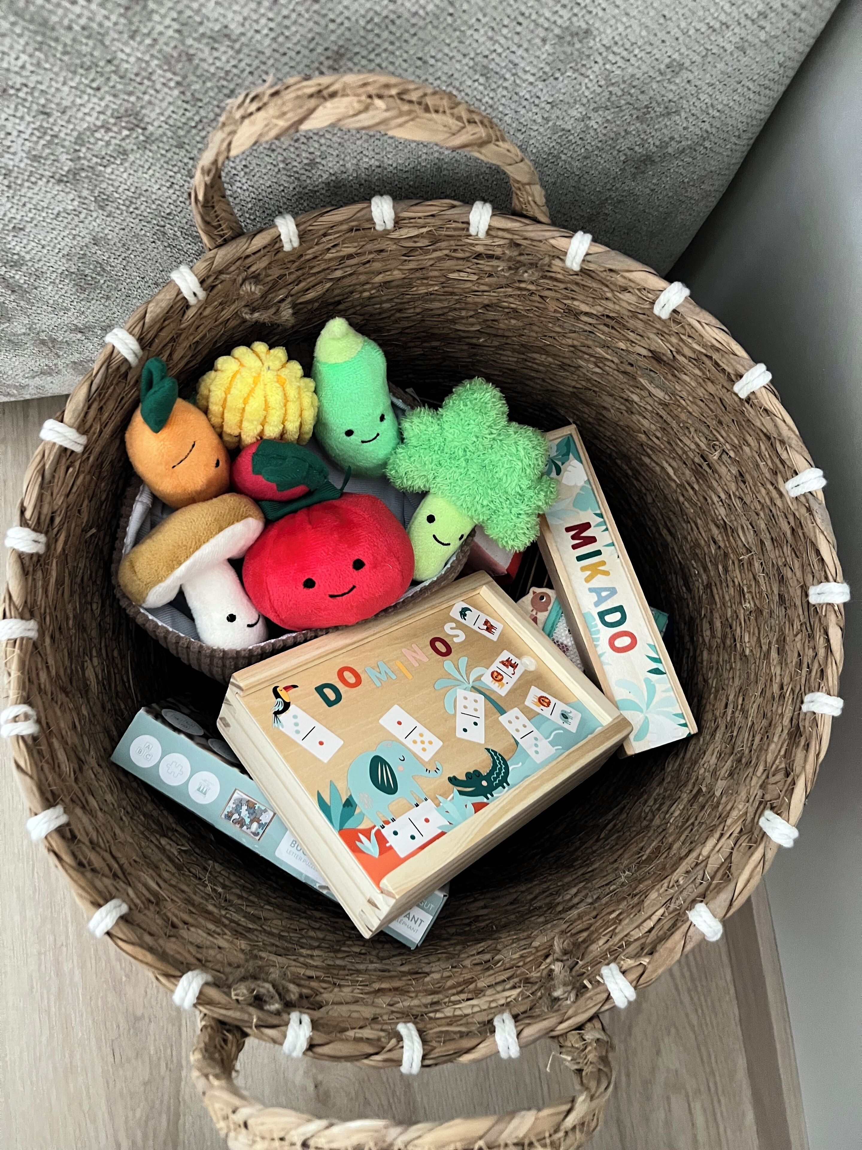 A wicker basket filled with plush toys and a wooden box labeled "DOMINOS".