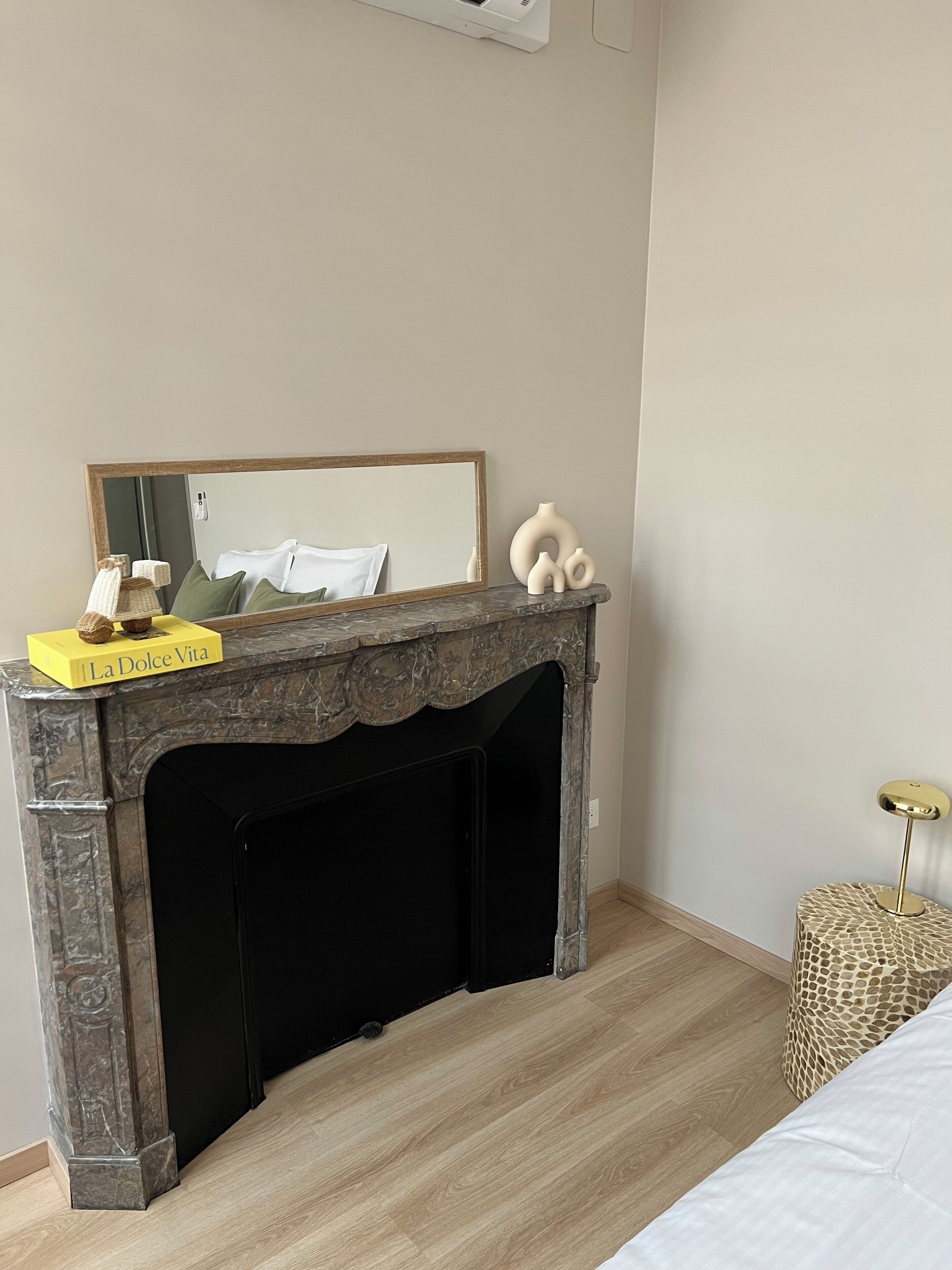 A bedroom with a marble fireplace, a bed, a bedside table, and a small round table with a lamp.