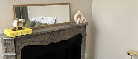 A bedroom with a marble fireplace, a bed, a bedside table, and a small round table with a lamp.
