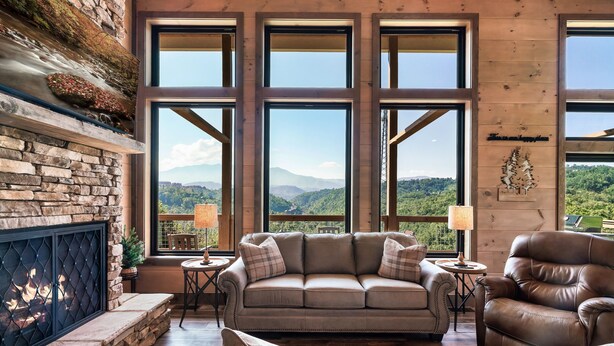 A cozy living room with a stone fireplace, large windows offering a mountain view, and comfortable seating.