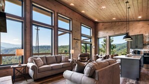 A spacious living room with large windows, a modern kitchen, and a view of the mountains.