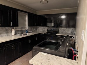Une cuisine avec des meubles de couleur noire, une cuisinière en acier inoxydable et un dosseret carrelé.