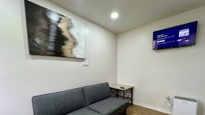 Una habitación moderna con un sofá gris, una mesita, un televisor de pantalla plana y un refrigerador pequeño.
