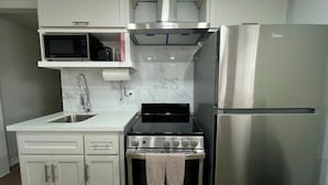 Una cocina compacta con muebles blancos, estufa de acero inoxidable, microondas y refrigerador.