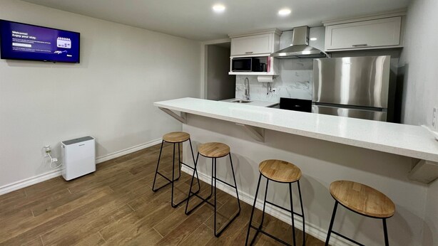 Una cocina moderna con encimera blanca, electrodomésticos de acero inoxidable y tres taburetes de madera.