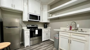 Una cocina moderna con armarios blancos, un refrigerador de acero inoxidable, un microondas, un horno y un lavamanos.