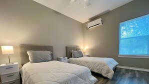 Un dormitorio con dos camas, una mesita de noche, una lámpara y un equipo de aire acondicionado.