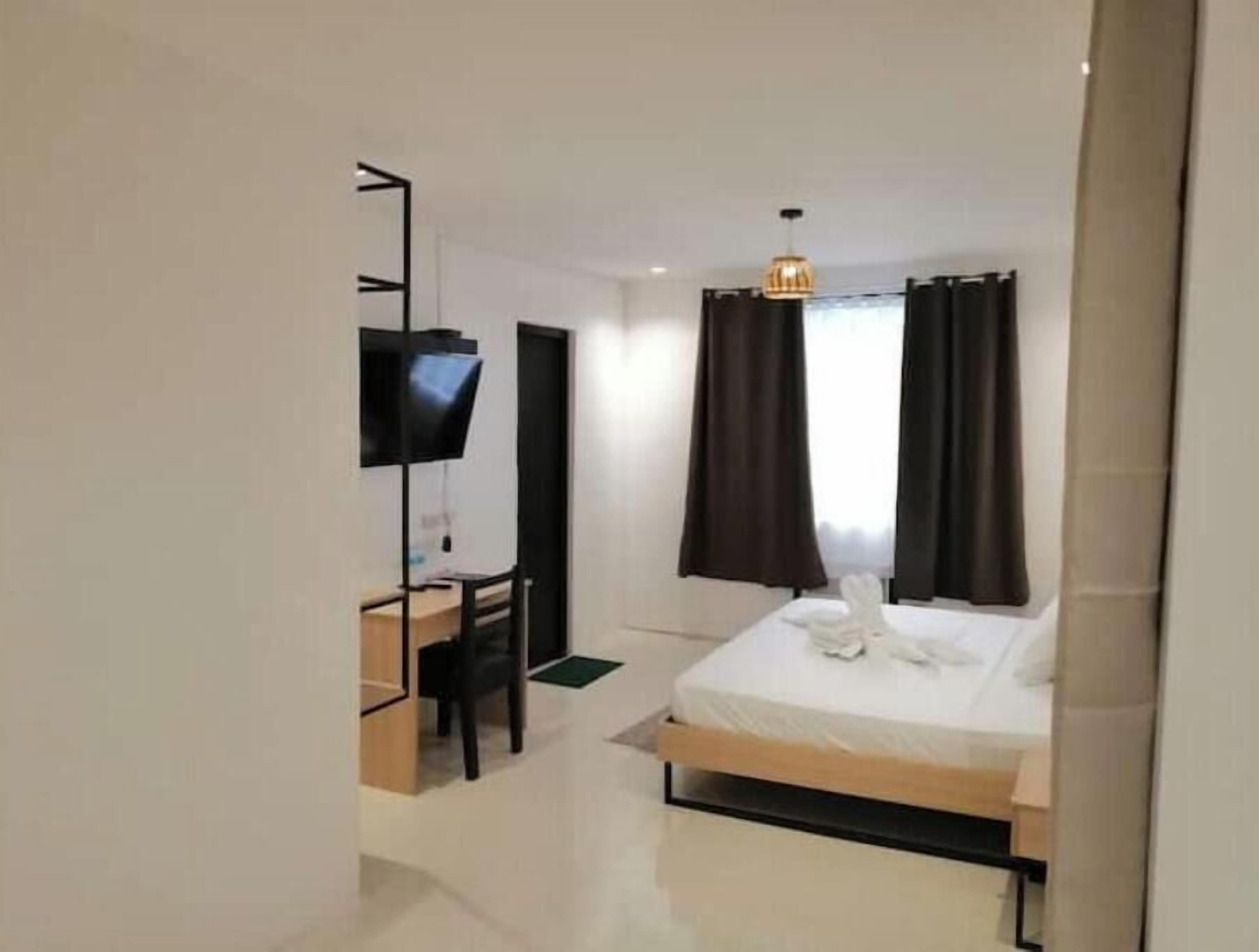 Una habitación de hotel con cama, escritorio, silla, televisor y cortinas.