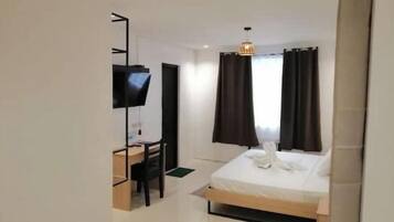 Una habitación de hotel con cama, escritorio, silla, televisor y cortinas.