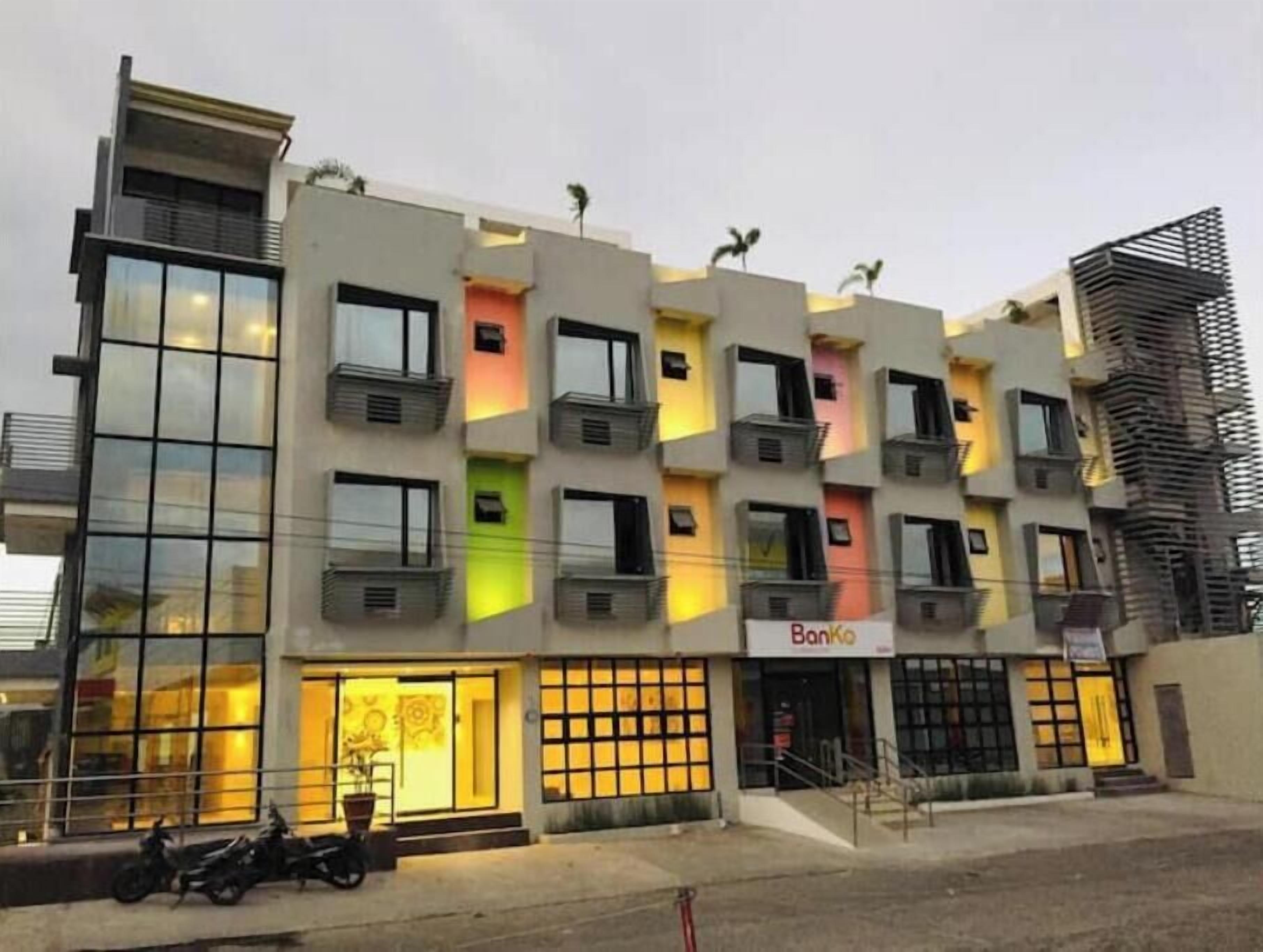 Un edificio a più piani con balconi, un cartello con la scritta 'Banko' e una motocicletta parcheggiata all'esterno.