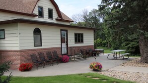 A two-story building with a brick foundation and a white upper section. There are outdoor seating arrangements with chairs and tables, and a picnic table.