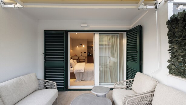 A balcony with two sofas and a small table, a sliding glass door leading to a bedroom with a bed and a nightstand, and a wall-mounted plant. - Terrace Haven Hvar (Hvar)