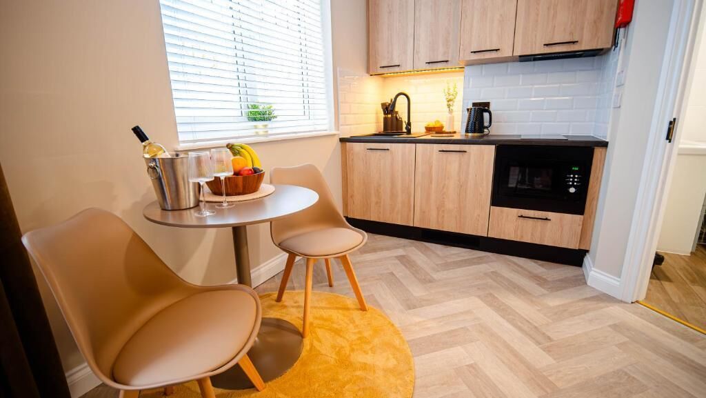 Eine kompakte Küche mit Holzschränken, einer Mikrowelle und einer kleinen Essecke mit zwei Stühlen und einem Tisch.