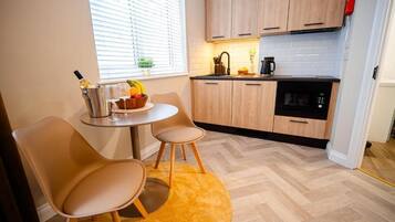 Eine kompakte Küche mit Holzschränken, einer Mikrowelle und einer kleinen Essecke mit zwei Stühlen und einem Tisch.