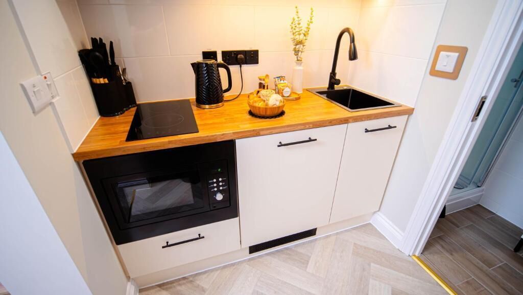A compact kitchen with a wooden countertop, a built-in oven, a sink, and white cabinetry.