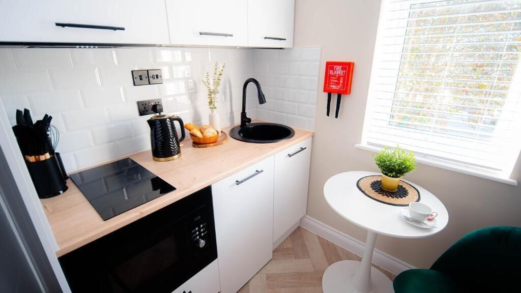 A compact kitchen with white cabinets, a black sink, and a small dining area with a white table and a potted plant.