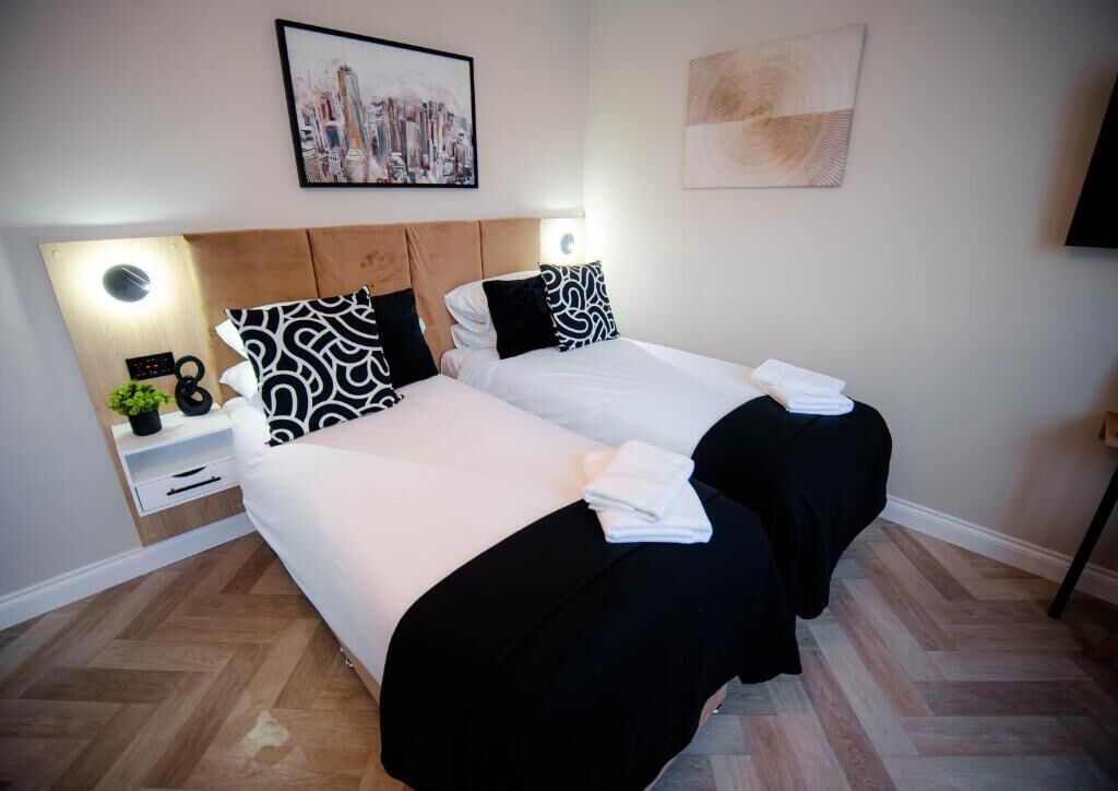 Una habitación de hotel con dos camas, una mesita de noche, un reloj y una pintura de un paisaje urbano.