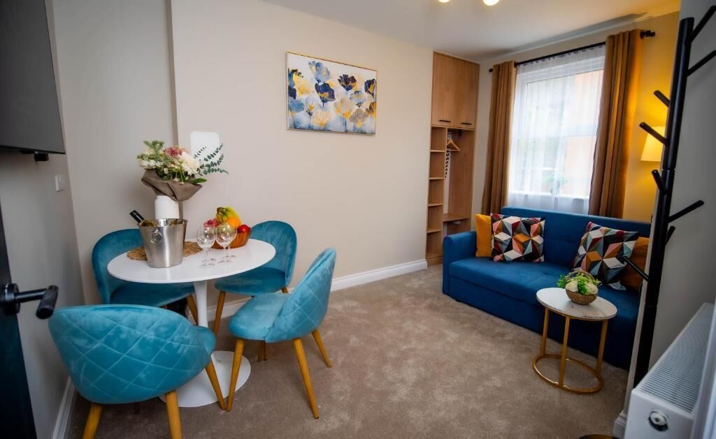Ein Wohnzimmer mit einem blauen Sofa, einem Esstisch mit Stühlen, einem kleinen Beistelltisch und einem Gemälde an der Wand.