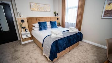 Une chambre à coucher comprenant un lit, des tables de chevet, une commode, une horloge murale, un tableau encadré et une fenêtre avec des rideaux.