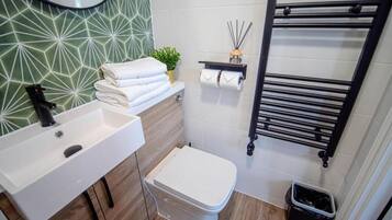 Ein modernes Badezimmer mit einem weißen Waschbecken, einer Holzwaschtisch-Konsole, einer weißen Toilette und einem schwarzen Handtuchhalter.
