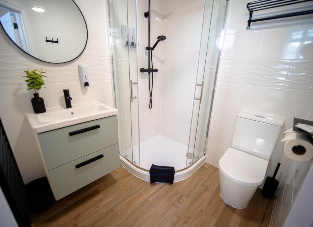 A modern bathroom with a glass-enclosed shower, a toilet, and a sink with a mirror.
