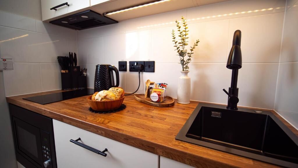 A modern kitchen with a wooden countertop, a black range hood, a vase with green plants, and a bread basket.