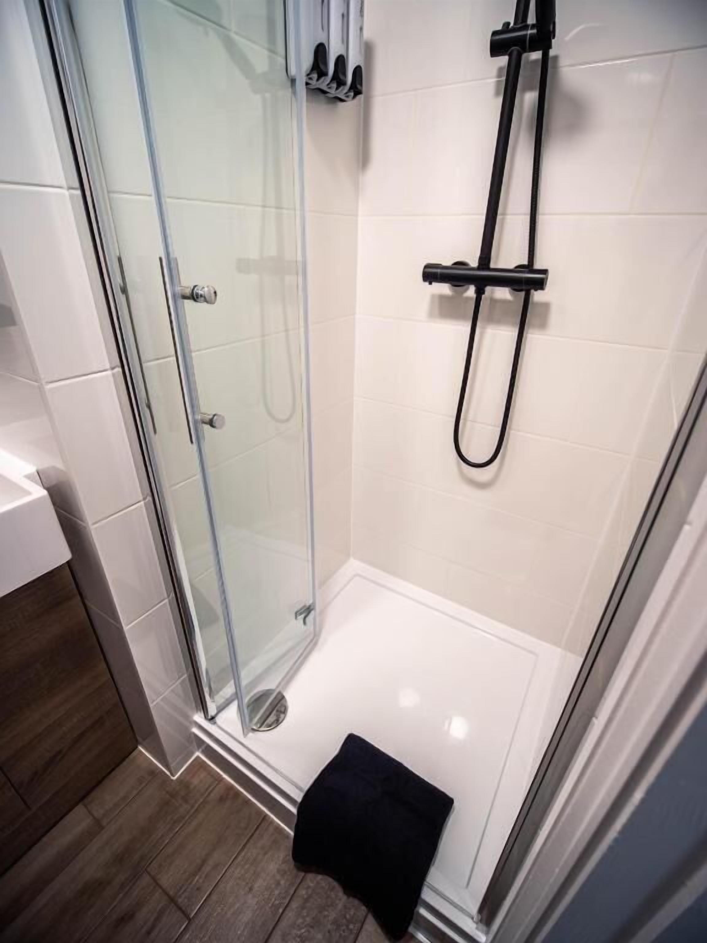 Een moderne douche met glazen douchecabine, handdouche en een wandmengkraan.