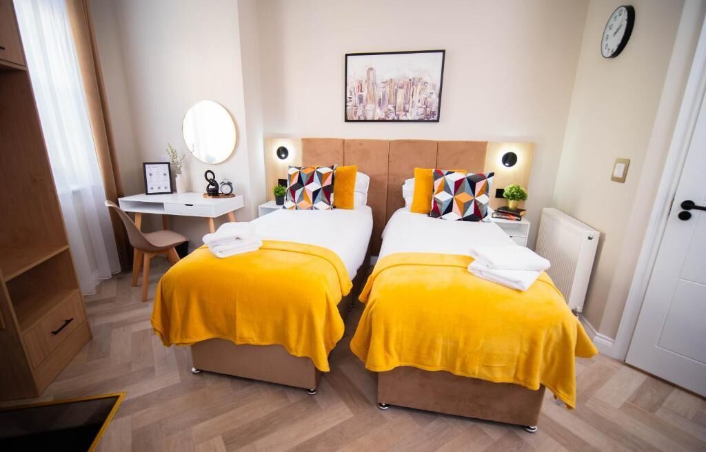 Camera d'albergo con due letti, una scrivania, una sedia, uno specchio e un quadro raffigurante un panorama urbano.