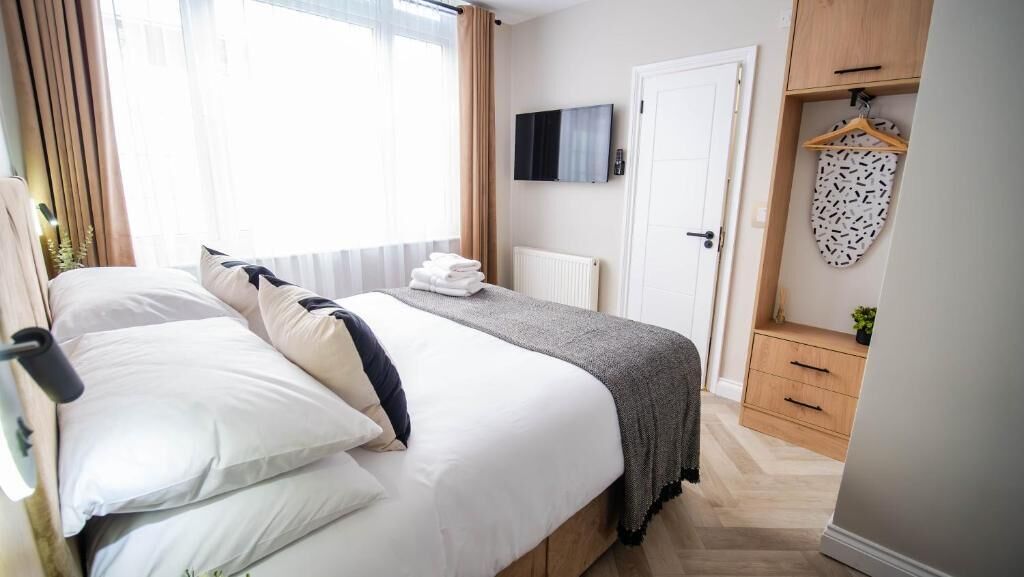 A hotel room with a bed, a TV mounted on the wall, a wardrobe, and a radiator.
