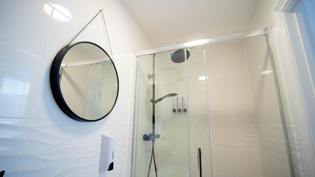A modern bathroom with a glass shower enclosure, a round mirror, and a towel rack.