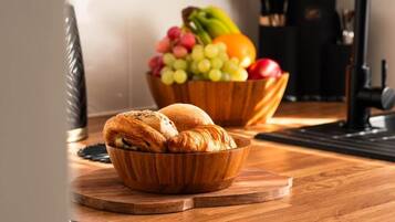 Puinen kulho, jossa on croissant-leivoksia, puisen leikkuulaudan päällä, ja taustalla toinen puinen kulho, jossa on hedelmiä.