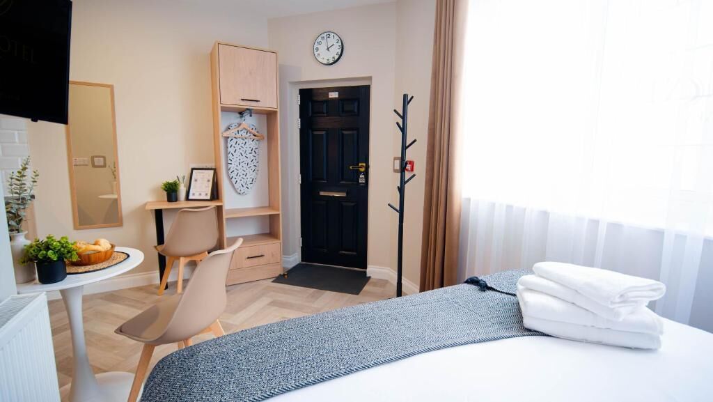 Hotelkamer met een bed, een bureau, een stoel, een kledingkast, een kapstok en een klok aan de muur.