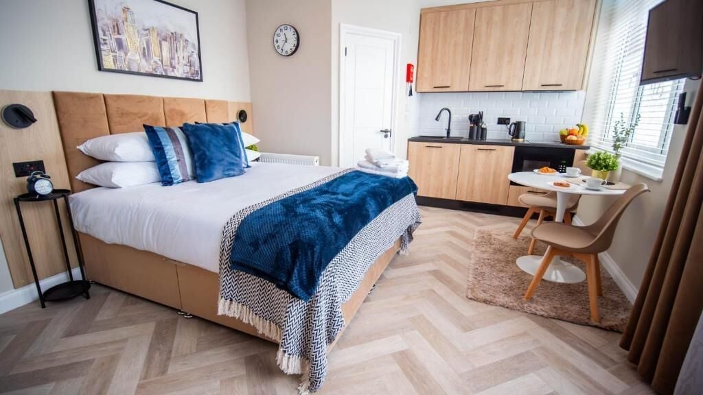A bedroom with a bed, bedside table, and a view of the kitchen.