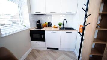 A compact kitchen with white cabinets, a black dishwasher, a sink, and a window with blinds.