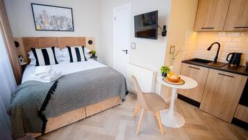 Une chambre d’hôtel comprenant un lit, une petite table avec une chaise, un coin cuisine et un tableau encadré au mur.