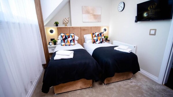 A hotel room with two beds, a TV, a clock, and a small table with a plant.