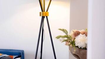 A modern living room with a black floor lamp with gold accents, a blue sofa with a geometric-patterned pillow, and a small round table with a candle and a vase of flowers.