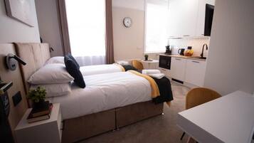 A hotel room with two beds, a small kitchenette, a desk, and a chair.