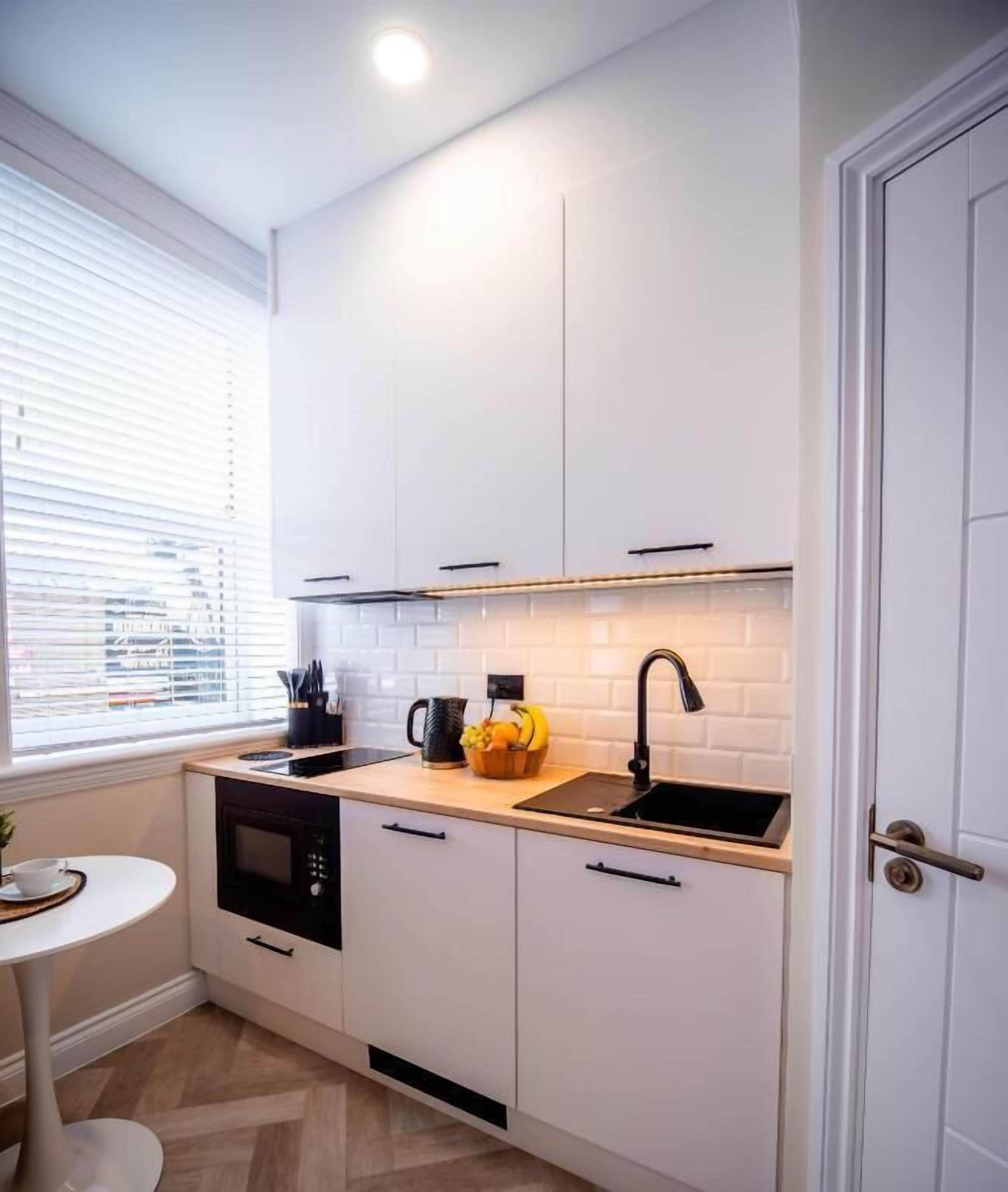 A compact kitchen with white cabinets, a black microwave, a sink, and a window with blinds.