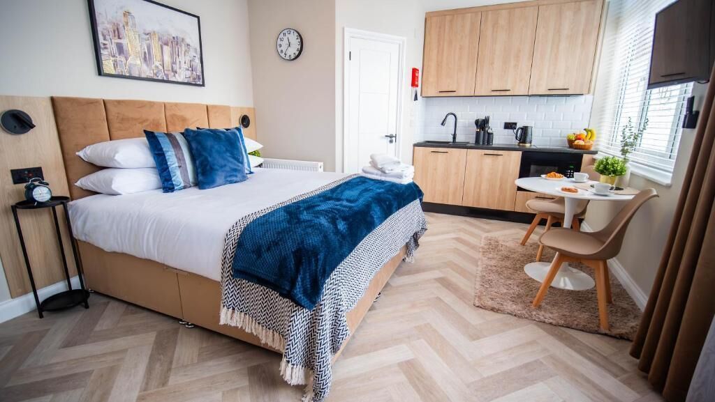 Une chambre à coucher comprenant un lit, une table de chevet et donnant sur un espace cuisine.