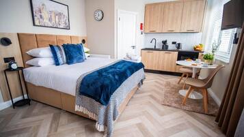 Une chambre à coucher comprenant un lit, une table de chevet et donnant sur un espace cuisine.