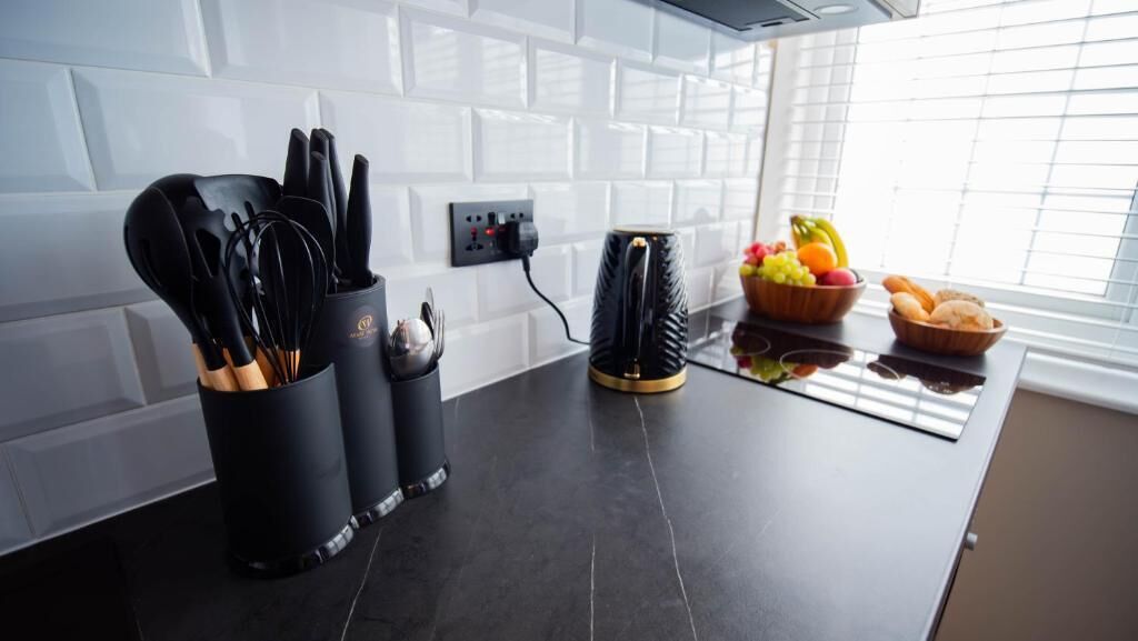 Een keuken met zwarte aanrechtbladen, een koffiezetapparaat en een schaal met fruit.