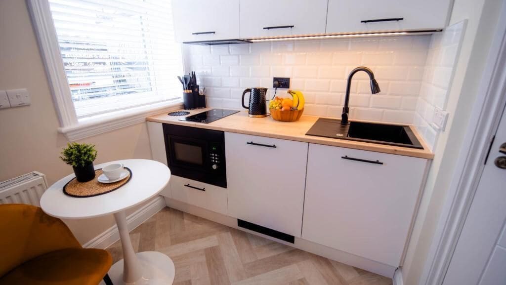 Eine kleine Küche mit weißen Schränken, einem schwarzen Herd, einer Spüle und einem Tisch mit einer Pflanze.