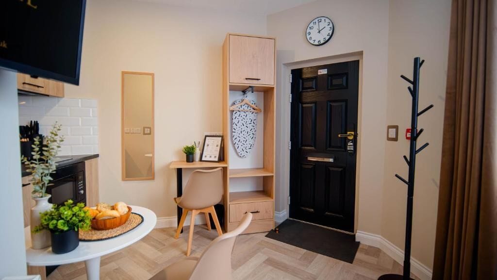 Un salon moderne avec un meuble en bois, une horloge, un porte-manteau et un coin repas comprenant une table et des chaises.
