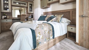A bedroom with a large bed, wooden headboard, built-in cabinets, a dresser, and a bedside table. - Lodge - Sleeps 4, Near Beach & Free Parking (New Quay)