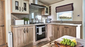 A modern kitchen with wooden cabinets, a built-in oven, a gas stove, and a large window. - Lodge - Sleeps 4, Near Beach & Free Parking (New Quay)