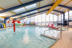 An indoor swimming pool with slides and a view of the outside.