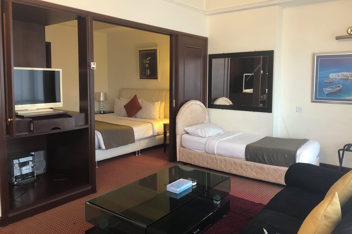 A hotel room with a bed, a sofa, a TV, a coffee table, and a desk with a computer.