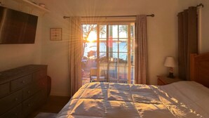 Une chambre à coucher comprenant un lit, un ventilateur de plafond, une table de chevet, une lampe, une commode et une fenêtre avec des rideaux.