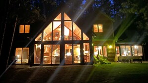 A large, modern house with a prominent glass facade, multiple windows, and a well-lit interior.